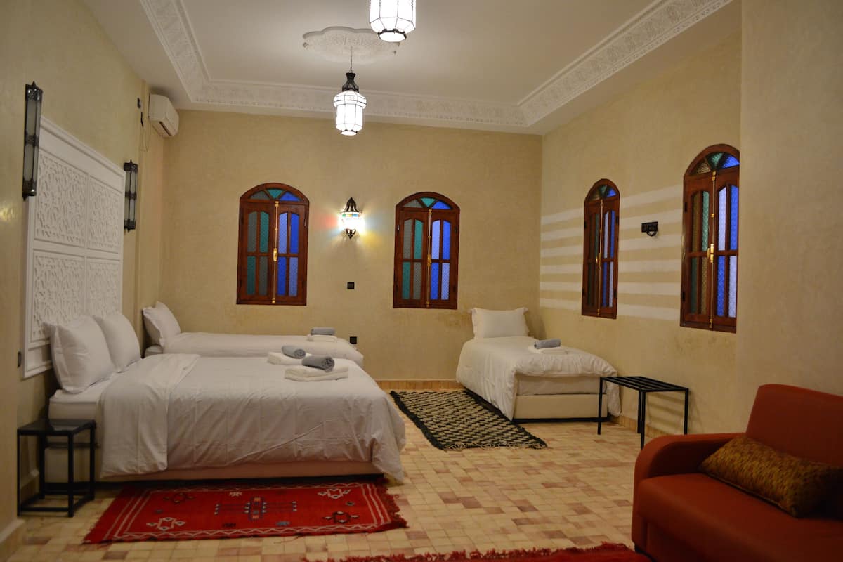 A hotel room with two beds, a red rug, a red sofa, and a small table.