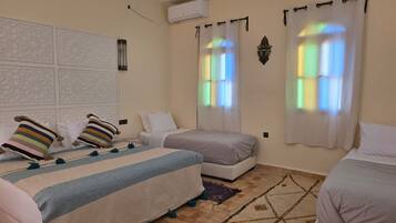 Un dormitorio con dos camas, un tapete estampado y un aire acondicionado de pared.