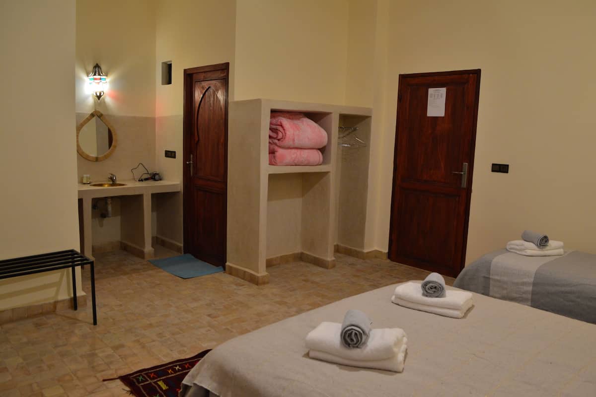 A hotel room with a bed, a bench, a mirror, a sink, and a shelf with folded towels.
