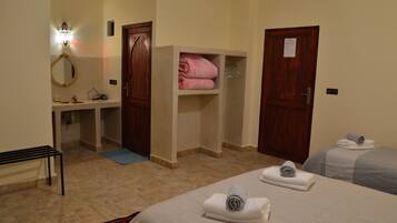 Une chambre d’hôtel avec un lit, un banc, un miroir, un lavabo et une étagère où sont pliées des serviettes.