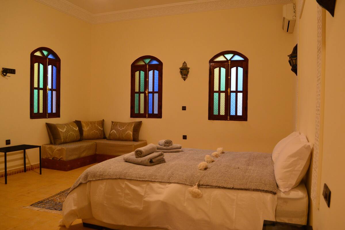 A bedroom with a bed, a sofa, and two stained glass windows.
