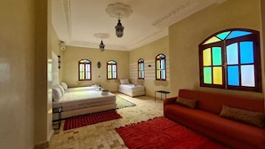 A spacious room with a large bed, a red sofa, and multiple windows with colorful stained glass. - KASBAH NTIFA (Ait Taguella)