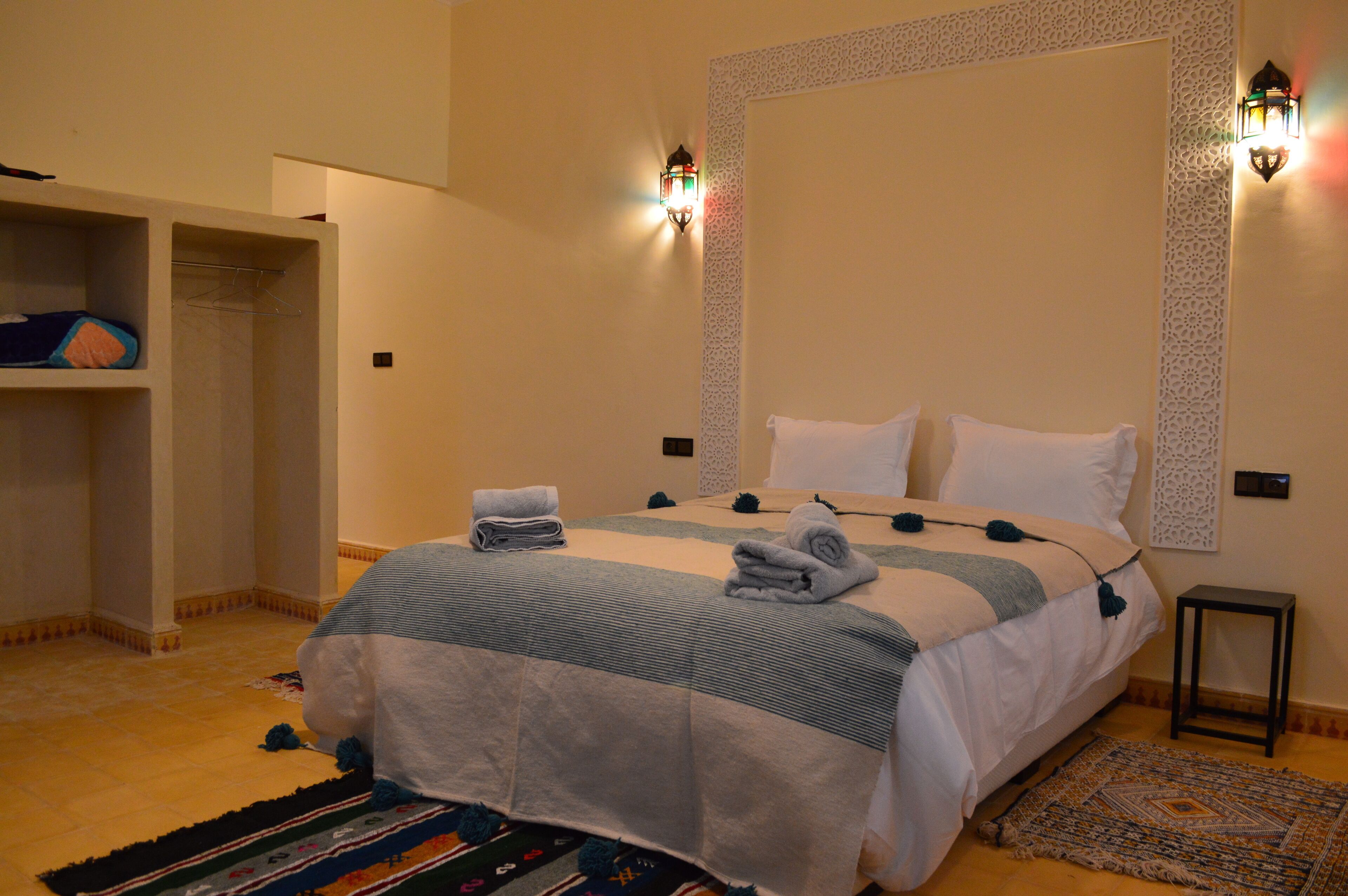 Una habitación de hotel con una cama, un armario, una mesita y apliques decorativos en la pared.