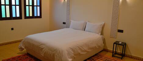 A bedroom with a bed, two wall-mounted lights, and a window with stained glass.