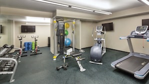 Un gimnasio con equipo de ejercicio diverso, incluyendo mancuernas, cinta de correr y máquina de pesas.