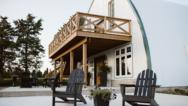Un edificio con terraza de madera, dos sillas Adirondack y una planta en maceta.