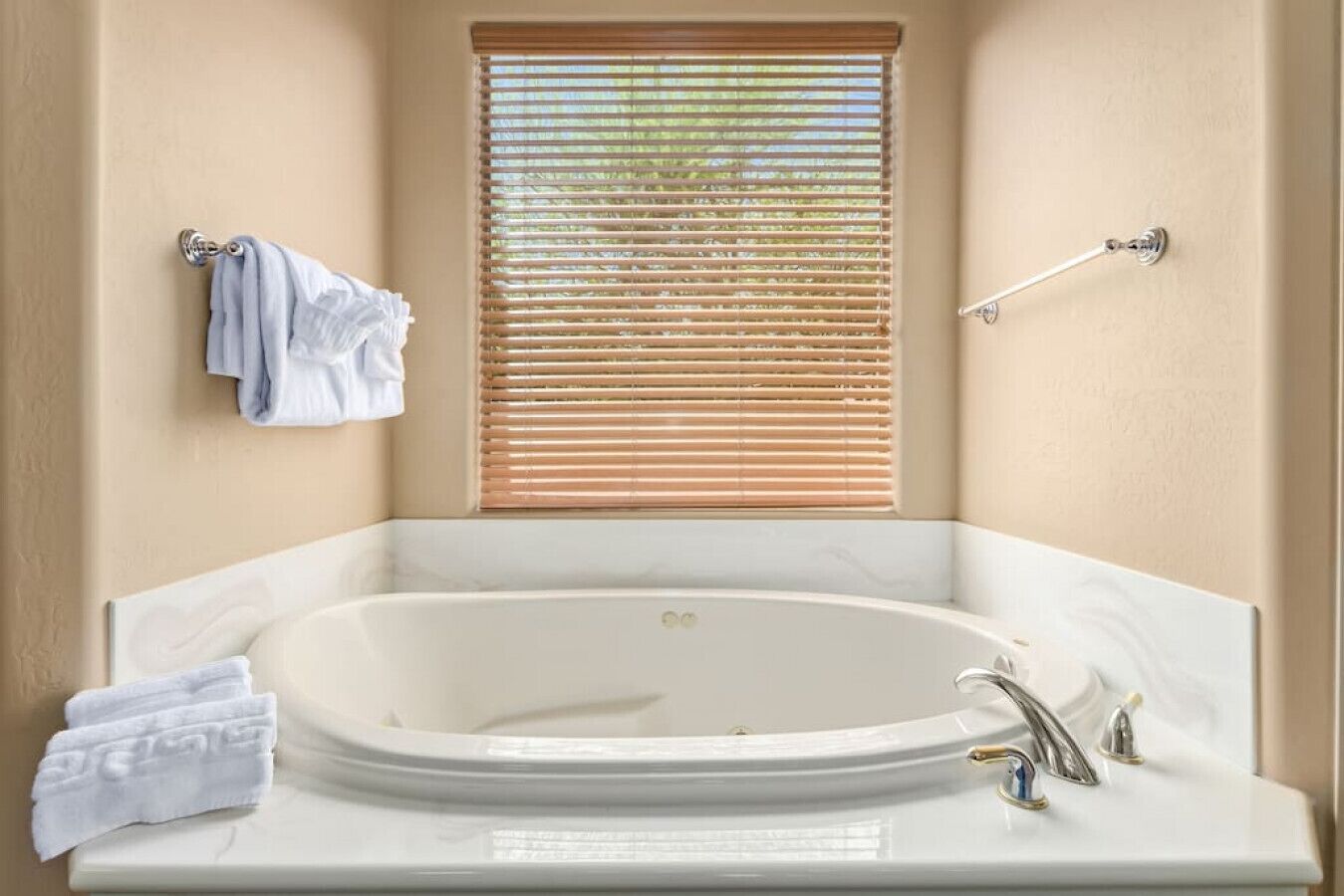 A bathroom with a freestanding bathtub, a window with blinds, and towels on a rack.