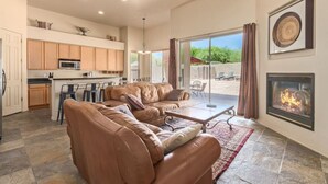 A spacious living room with a leather sofa, a fireplace, and a kitchen area with wooden cabinets and a microwave. - Troon/Gated/Pool/Firepit/Sleep 6 (Scottsdale)