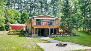 A two-story house with a balcony, a fire pit, and a red shed in a forested area. - Waterfront Eagle River Home w/ Dock + Fire Pit! (Eagle River)