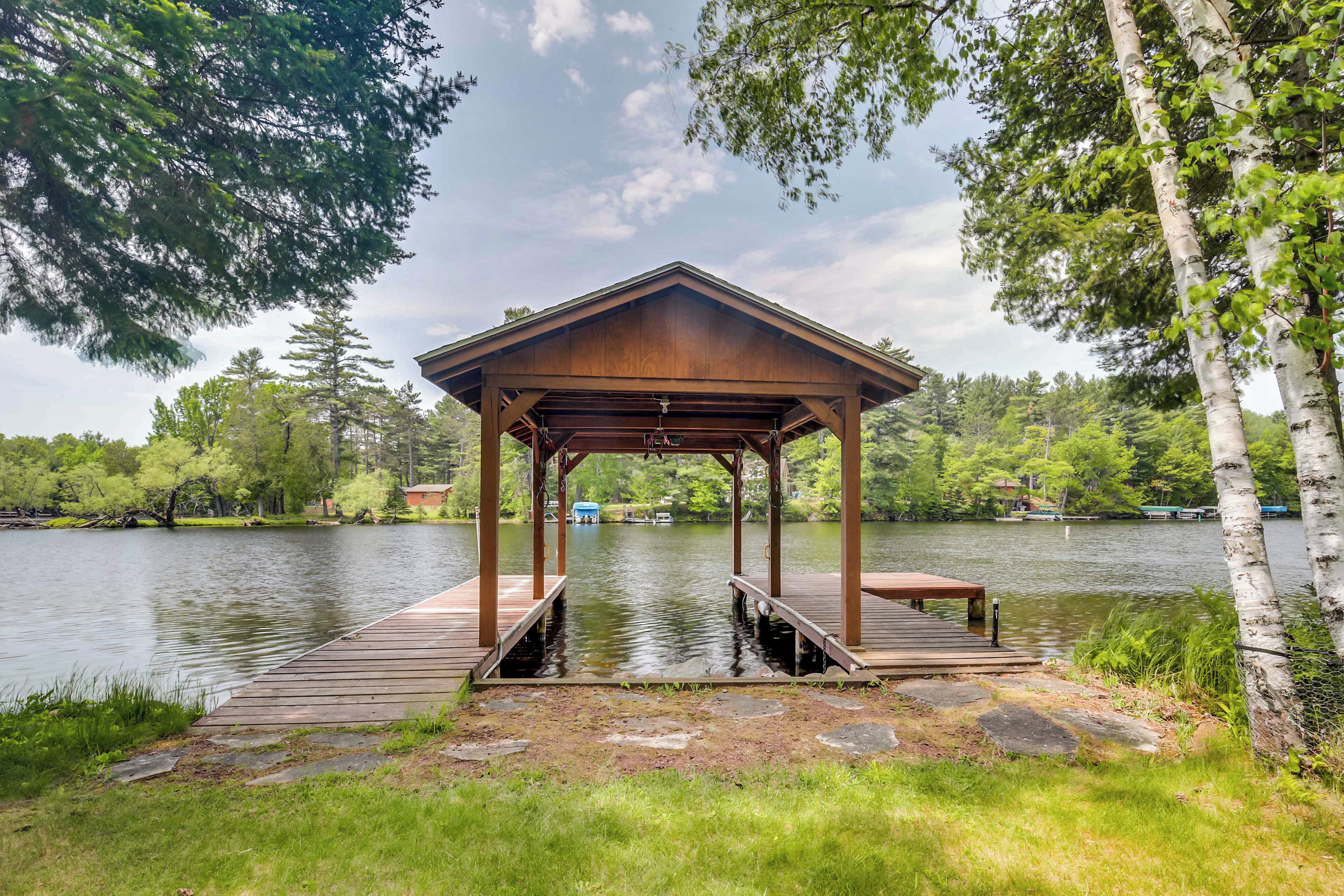 A wooden gazebo with a bench, overlooking a calm lake, surrounded by trees.