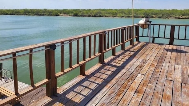 A wooden pier extending over calm turquoise water, with a metal railing and a sign on a pole. - Salty River Lodge Arroyo City, TX (Cameron County)