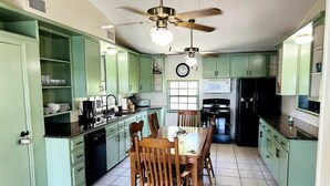 A kitchen with teal cabinets, a dining table with chairs, a ceiling fan, and a clock on the wall. - Salty River Lodge Arroyo City, TX (Cameron County)