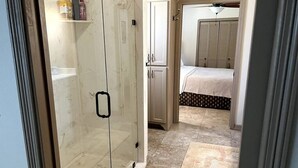 A bathroom with a glass shower enclosure, a white cabinet, and a bed with a patterned bedspread in the background. - Salty River Lodge Arroyo City, TX (Cameron County)