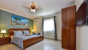 A bedroom with a bed, bedside tables, a ceiling fan, a painting, and a wardrobe.