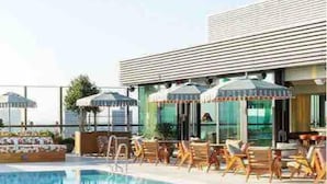 Ein Schwimmbecken mit Liegestühlen und Sonnenschirmen, ein modernes Gebäude mit großen Fenstern und ein klarer Himmel.