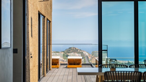 A balcony with wooden furniture and a view of a coastal town.