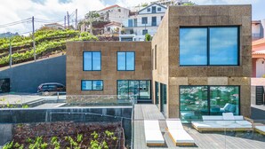 A modern building with a terrace featuring lounge chairs and a glass railing.