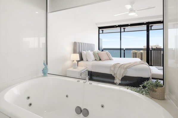 A modern bedroom with a large window, a bathtub, and a bed with pillows and a blanket.