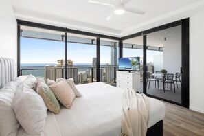 A modern bedroom with a large bed, a TV, and a balcony with a city view.