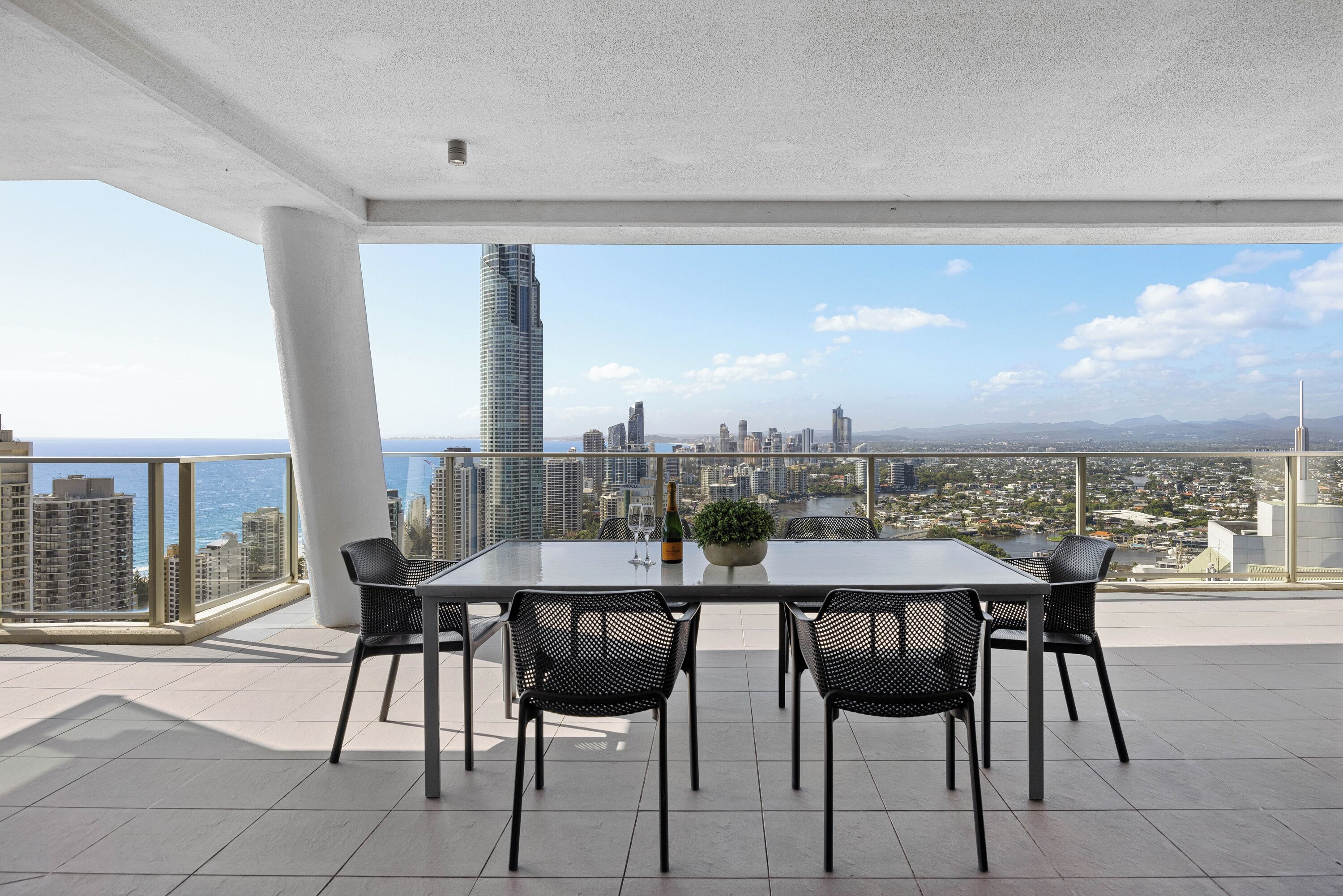 A balcony with a table and chairs, a bottle of champagne, and a potted plant.