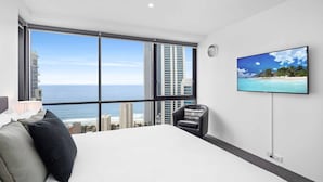 Habitación de hotel moderna con un ventanal amplio que ofrece vistas a la ciudad, una cama, un televisor y una silla.