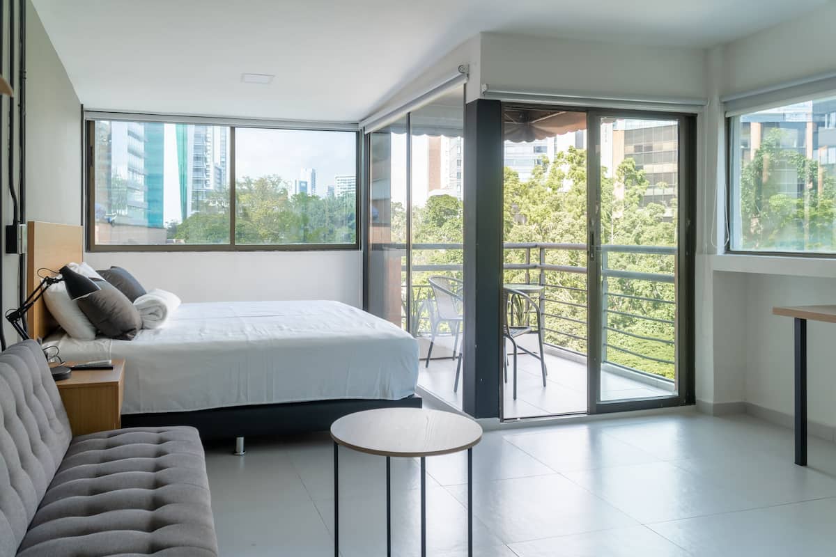 Une chambre moderne avec un grand lit, un canapé, une petite table ronde et un balcon offrant une vue sur la ville.
