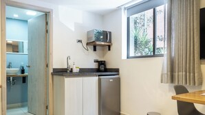 A compact kitchen with a microwave, coffee maker, and a small refrigerator. A window provides natural light, and a trash can is visible. - HOTEL BAMBU MILLA DE ORO (Medellín)