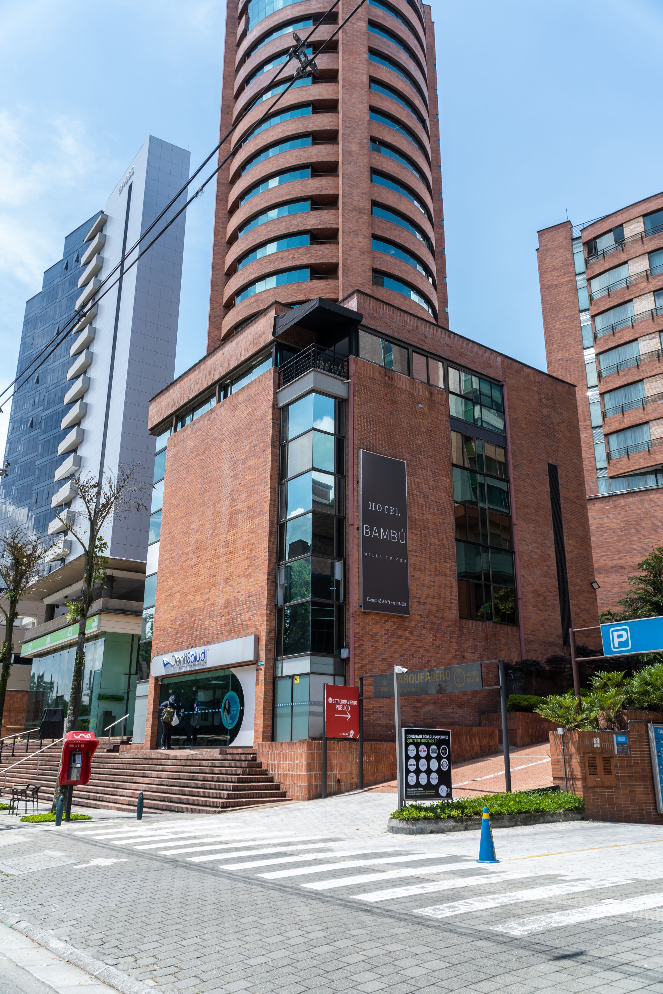 Un moderno edificio de hotel con un llamativo letrero que dice 'Hotel Bambú', una escalera que lleva a la entrada y un cartel de estacionamiento cerca.