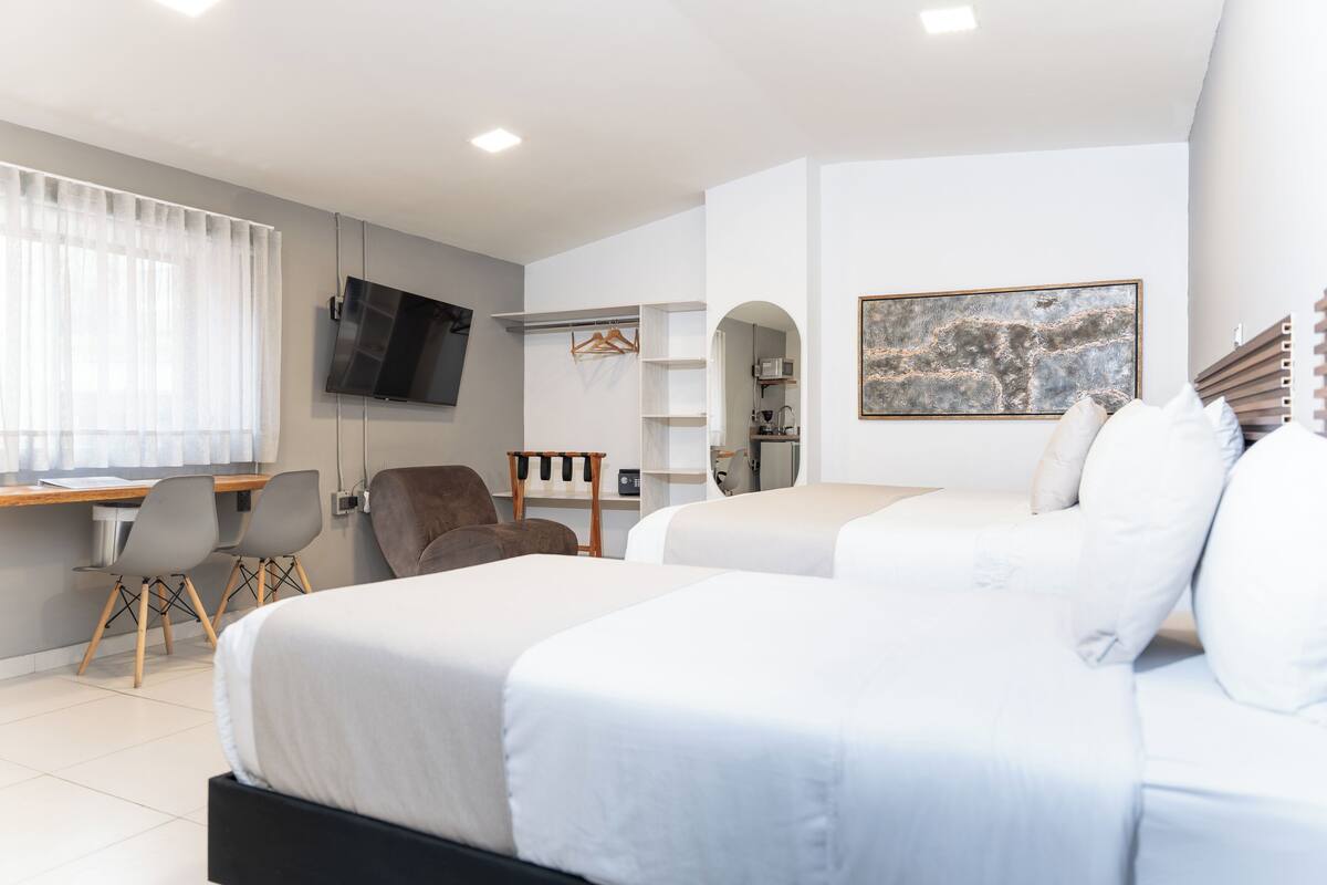 Une chambre d’hôtel moderne avec deux lits, un bureau, une télévision et un tableau au mur.
