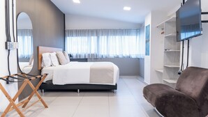 A modern bedroom with a bed, a chair, a TV, and a window with curtains. - HOTEL BAMBU MILLA DE ORO (Medellín)