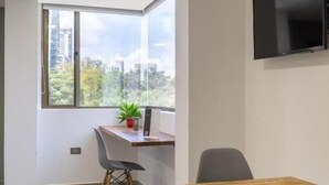 A modern room with a large window, a flat-screen TV, and a wooden table. - HOTEL BAMBU MILLA DE ORO (Medellín)
