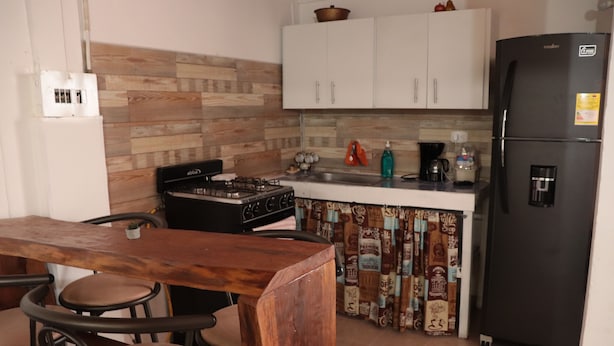 Une cuisine avec une table en bois, des tabourets de bar, une cuisinière, des placards et un réfrigérateur.