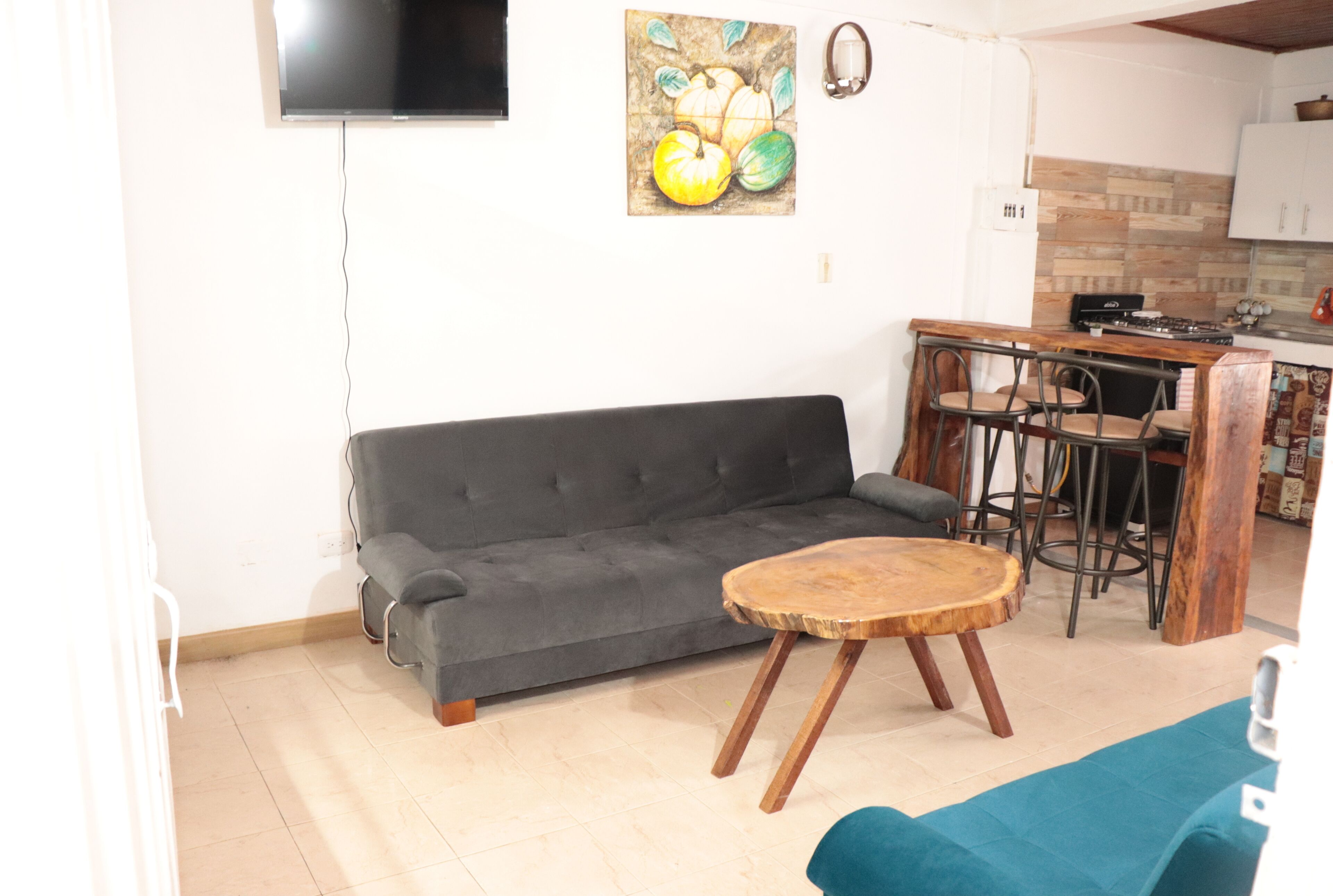 A living room with a grey sofa, a round wooden coffee table, and a TV mounted on the wall.