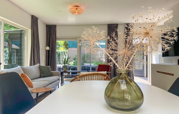 Un salón moderno con un jarrón de vidrio sobre una mesa blanca, un sofá y una zona de comedor.