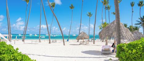 A beach with palm trees, a thatched-roof hut, and a beach chair.