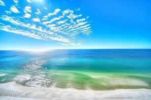 Ein Strand mit klarem türkisblauem Wasser und einem sandigen Ufer unter einem strahlend blauen Himmel mit vereinzelten Wolken.