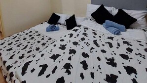 Een slaapkamer met een bed, voorzien van een zwart-wit koeienprint deken, een hoofdbord en meerdere kussens.