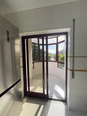 A hallway with a glass door leading to an outdoor area with a view of buildings and greenery.