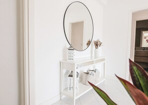 A white console table with a mirror above it, a small lamp, and decorative items.