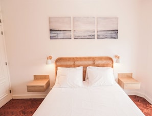 A bedroom with a large bed, two nightstands, a wicker headboard, and a wall-mounted painting.