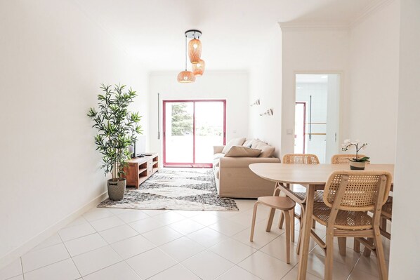 A modern living room with a sofa, a dining table with chairs, a potted plant, and a hanging light fixture.