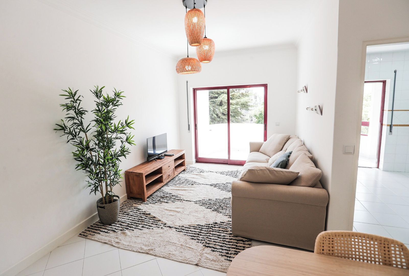 Un salon avec un canapé, un téléviseur posé sur un meuble en bois, une plante en pot et une grande fenêtre donnant sur un beau paysage.