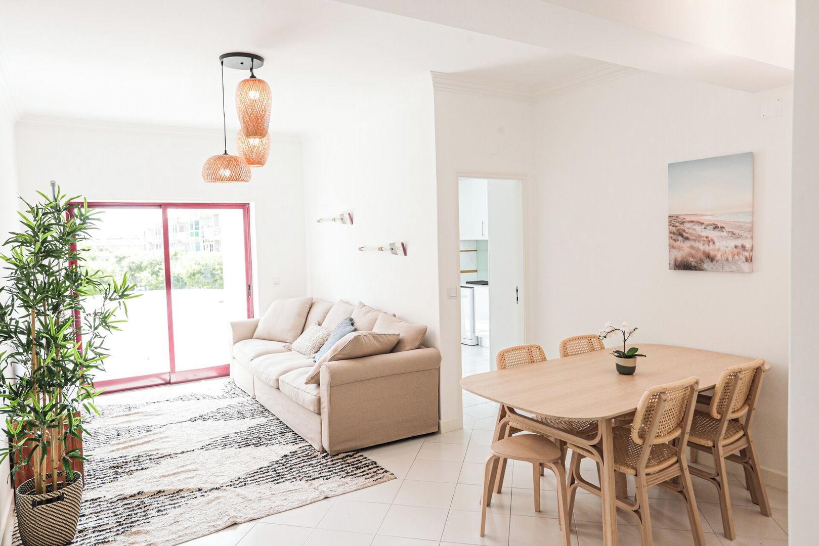 A modern living room with a sofa, dining table, chairs, a potted plant, and a hanging light fixture.