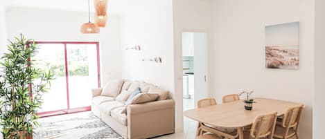 A modern living room with a sofa, dining table, chairs, a potted plant, and a hanging light fixture.