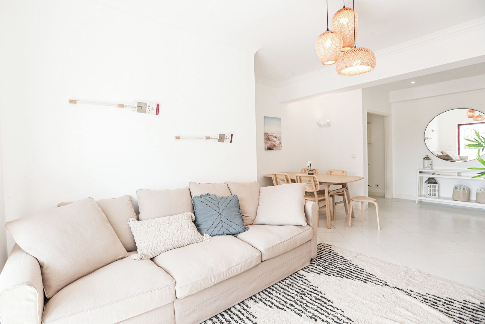 A modern living room with a beige sofa, a dining table with chairs, and a large mirror.