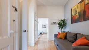 Una sala de estar moderna con un sofá gris, cojines naranjas, una planta y un cuadro en la pared.