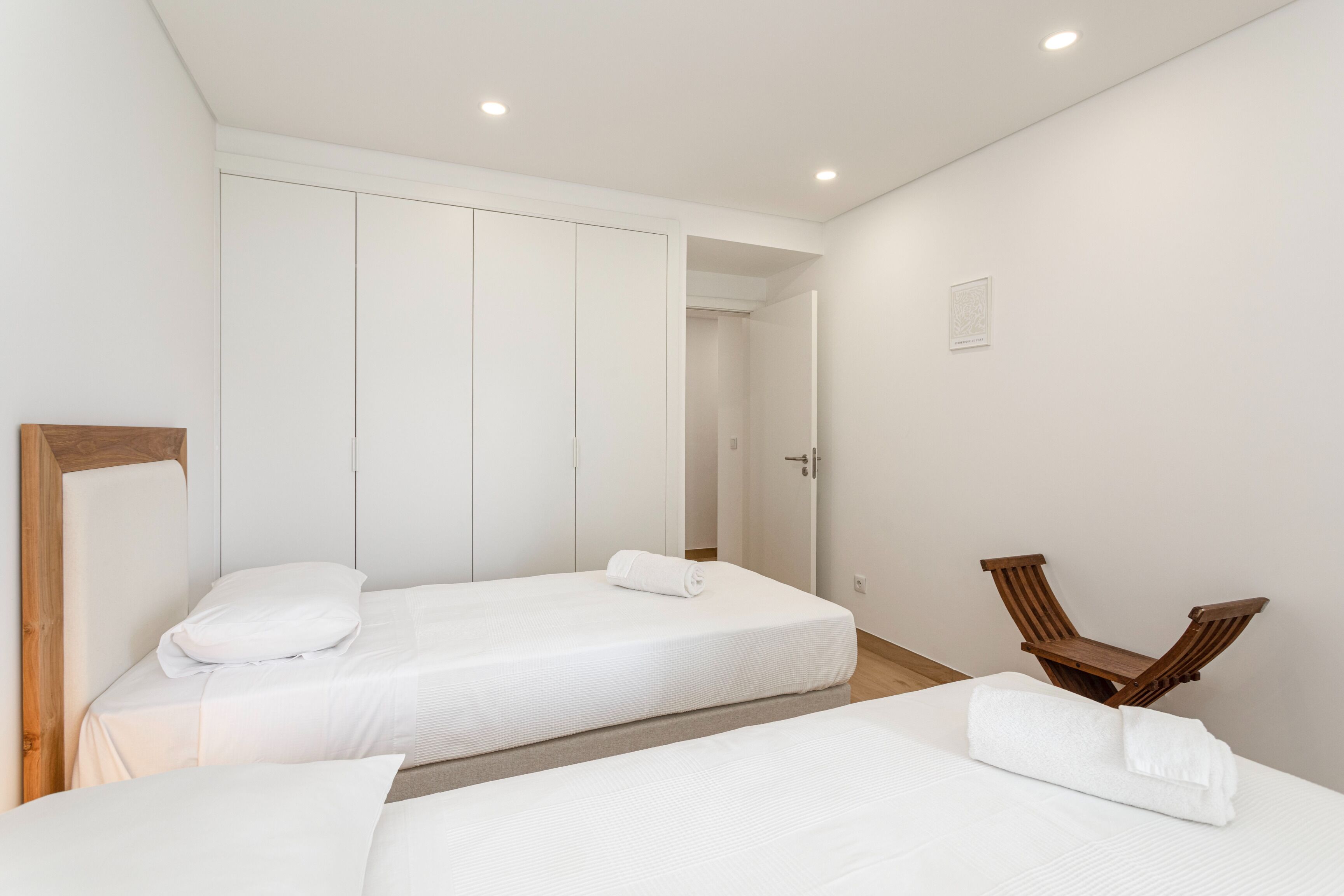 A hotel room with two beds, a wooden chair, and a wardrobe.