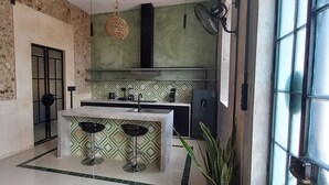 Una cocina moderna con una isla central, dos taburetes de bar, una lámpara colgante y un amplio ventanal.