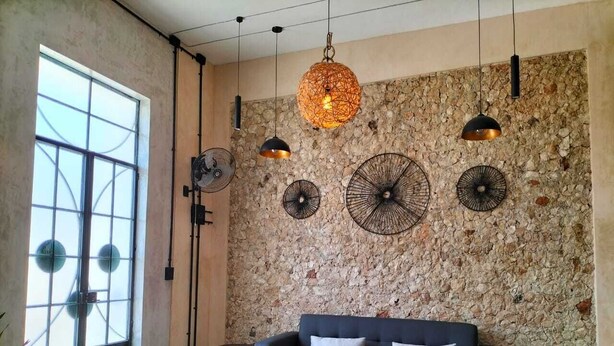 Una sala de estar moderna con una pared de piedra, un sofá oscuro y múltiples lámparas colgantes.