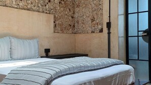 Un dormitorio moderno con pared de piedra, una cama grande con estructura de madera y vistas al exterior por una ventana.